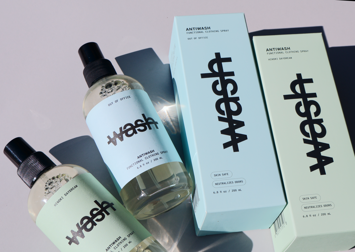 two full size antiwash bottles in hinoki daydream and out of office laid on a grey surface next to their corresponding boxes 