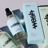 two full size antiwash bottles in hinoki daydream and out of office laid on a grey surface next to their corresponding boxes 