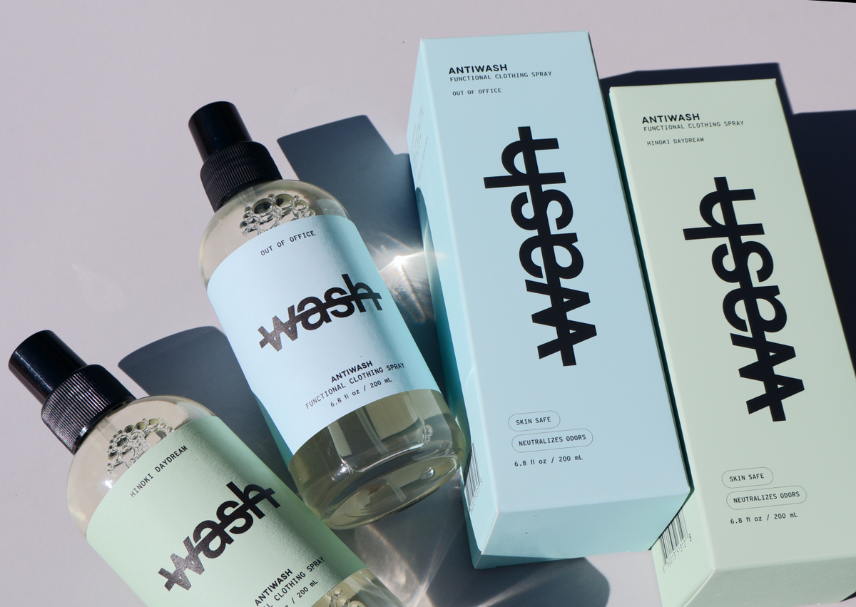 two full size antiwash bottles in hinoki daydream and out of office laid on a grey surface next to their corresponding boxes 