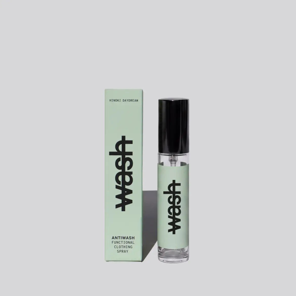 A clear 15ml glass spray bottle with a black cap stands next to its matching light green box. Both the bottle and box feature the word 'wash' in large black vertical letters and are labeled as antiwash functional clothing spray 